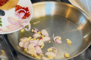 Cook garlic, shallots, and sliced red chili pepper for Garlic Clam and Shrimp Pasta